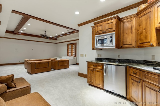 kitchen featuring stainless steel microwave, dark stone counters, crown molding, fridge, and light colored carpet