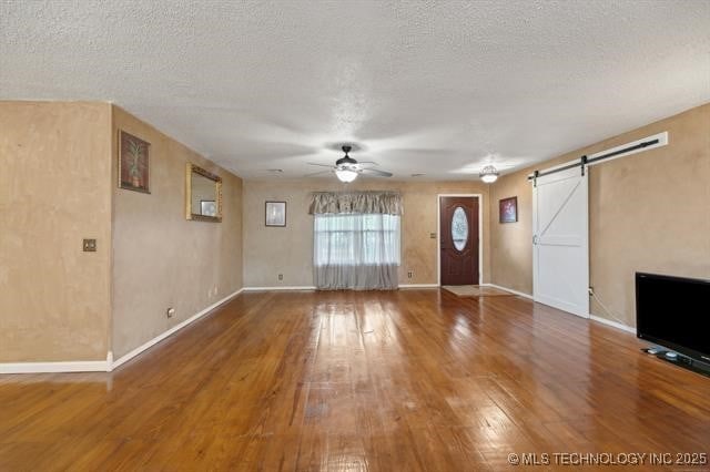 unfurnished living room with ceiling fan, wood-type flooring, a textured ceiling, and a barn door