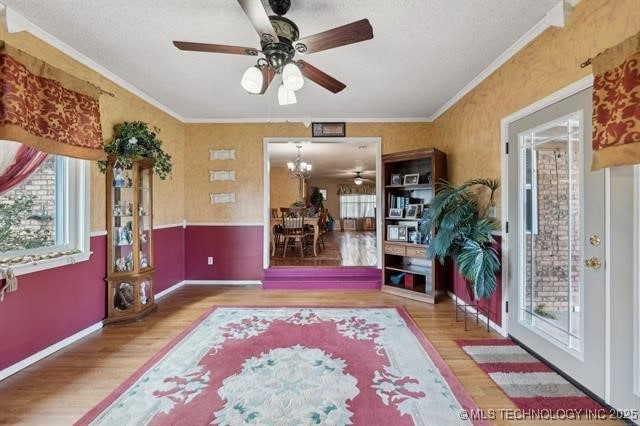 living area with crown molding, wood-type flooring, ceiling fan with notable chandelier, and a textured ceiling