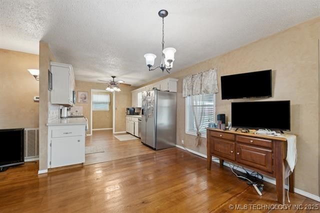 kitchen featuring white cabinetry, stainless steel fridge with ice dispenser, hardwood / wood-style floors, ceiling fan with notable chandelier, and a textured ceiling