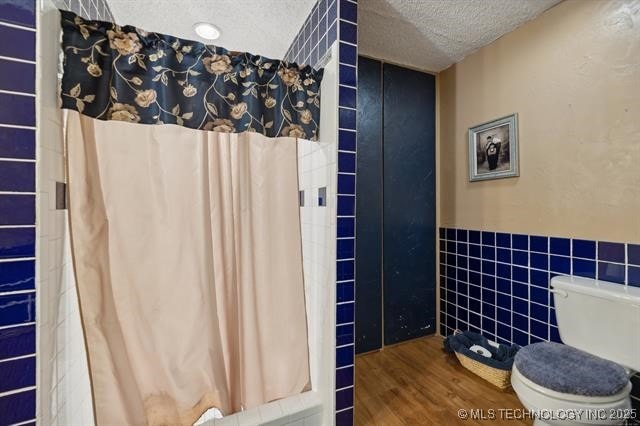 bathroom with wood-type flooring, a textured ceiling, toilet, and tile walls