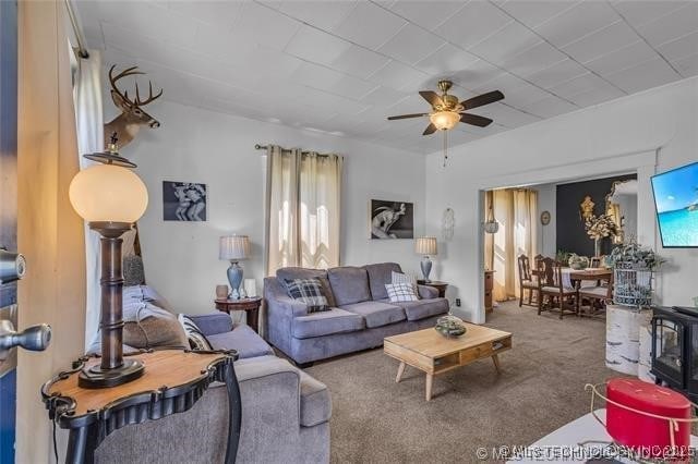 carpeted living room with ceiling fan and a wood stove