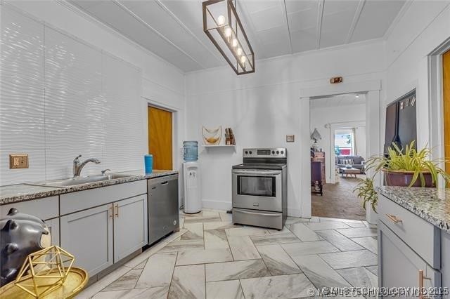 kitchen featuring gray cabinetry, sink, light stone counters, crown molding, and appliances with stainless steel finishes