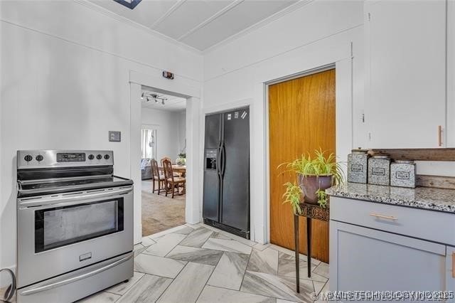 kitchen with gray cabinetry, light stone countertops, black refrigerator with ice dispenser, stainless steel electric stove, and ornamental molding