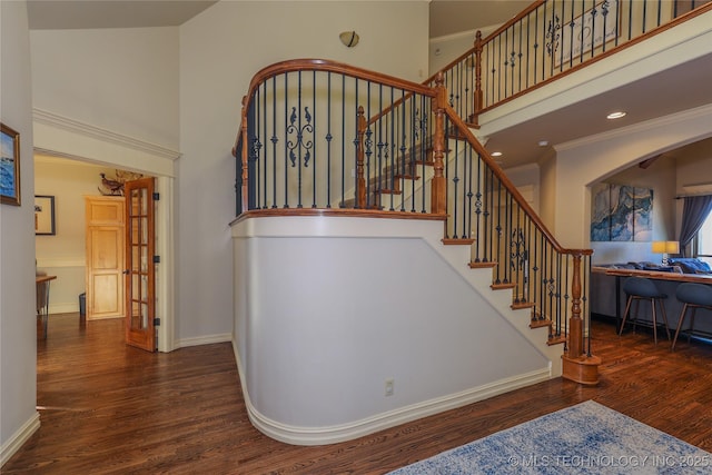 staircase with hardwood / wood-style flooring, a towering ceiling, and ornamental molding