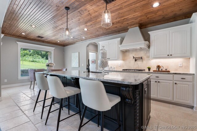 2787 Forest View Dr, Claremore, OK 74017 - kitchen featuring premium range hood, wooden ceiling, decorative backsplash, white cabinetry, and an island with sink