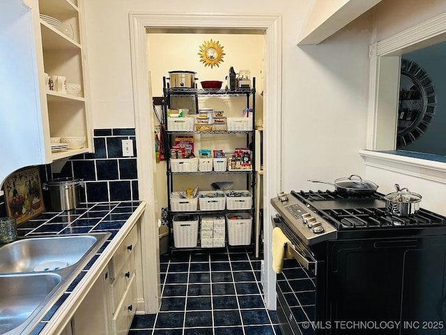 kitchen featuring decorative backsplash, gas stove, dark tile patterned floors, sink, and tile countertops