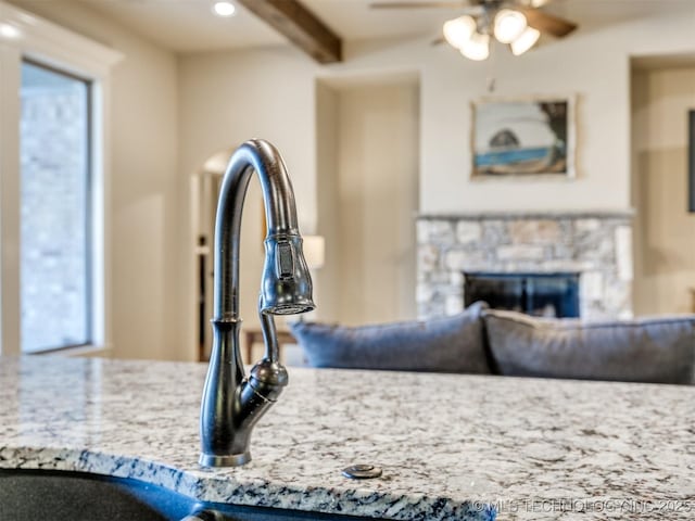 room details with beamed ceiling, a stone fireplace, and ceiling fan