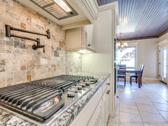 kitchen featuring an inviting chandelier, tasteful backsplash, light stone counters, white cabinetry, and stainless steel gas cooktop