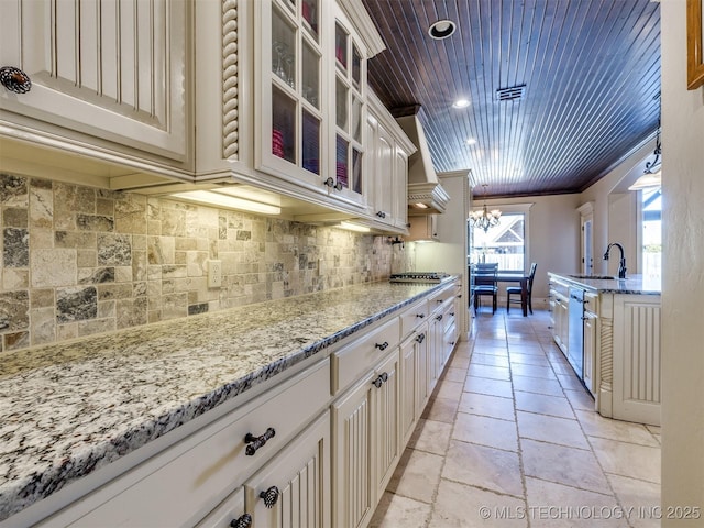 kitchen with light stone countertops, crown molding, sink, decorative light fixtures, and an inviting chandelier