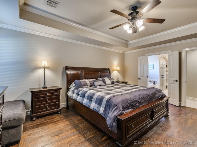 bedroom featuring dark hardwood / wood-style flooring, ensuite bathroom, ornamental molding, a raised ceiling, and ceiling fan