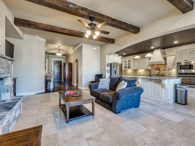 living room with ceiling fan, beam ceiling, and a stone fireplace