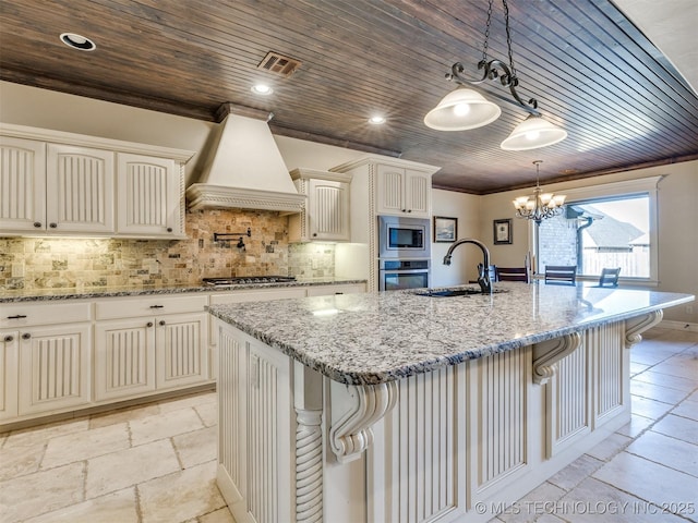 kitchen with decorative backsplash, custom range hood, sink, a center island with sink, and decorative light fixtures