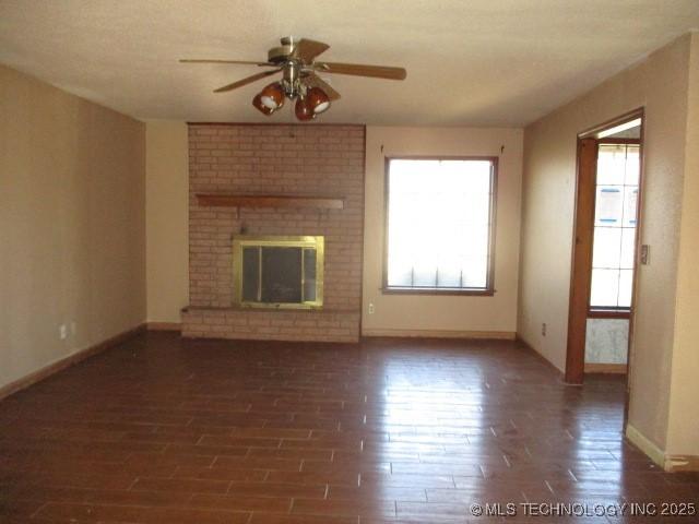 unfurnished living room with ceiling fan, dark hardwood / wood-style flooring, and a brick fireplace