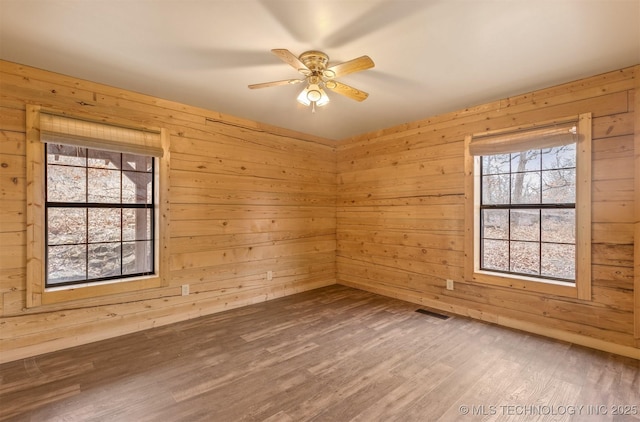 unfurnished room with wooden walls, hardwood / wood-style floors, and ceiling fan