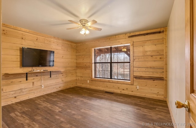 unfurnished living room with wooden walls, ceiling fan, and dark wood-type flooring