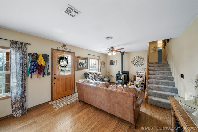 living room with ceiling fan, a wood stove, and light hardwood / wood-style flooring