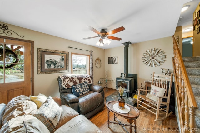 living room with a wood stove, ceiling fan, and wood-type flooring