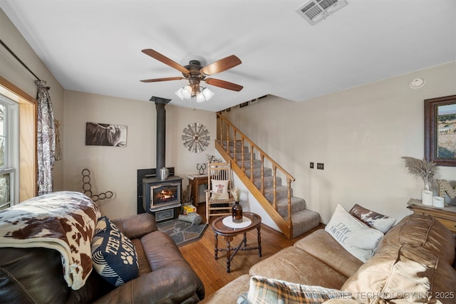 living room with ceiling fan, wood-type flooring, and a wood stove