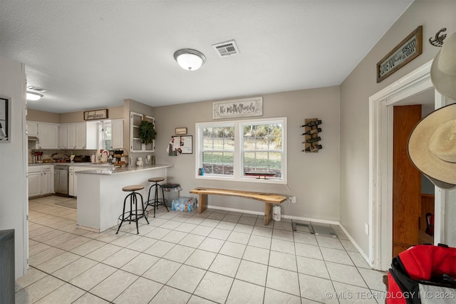 kitchen with kitchen peninsula, stainless steel dishwasher, white cabinetry, a breakfast bar area, and light tile patterned flooring