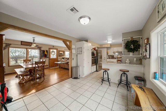 kitchen with kitchen peninsula, stainless steel oven, white cabinets, a breakfast bar area, and light tile patterned flooring