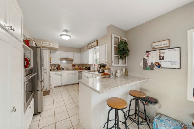 kitchen with a kitchen bar, kitchen peninsula, backsplash, stainless steel appliances, and white cabinets