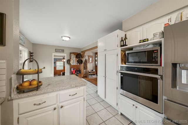 kitchen featuring light stone countertops, white cabinets, light tile patterned flooring, and appliances with stainless steel finishes