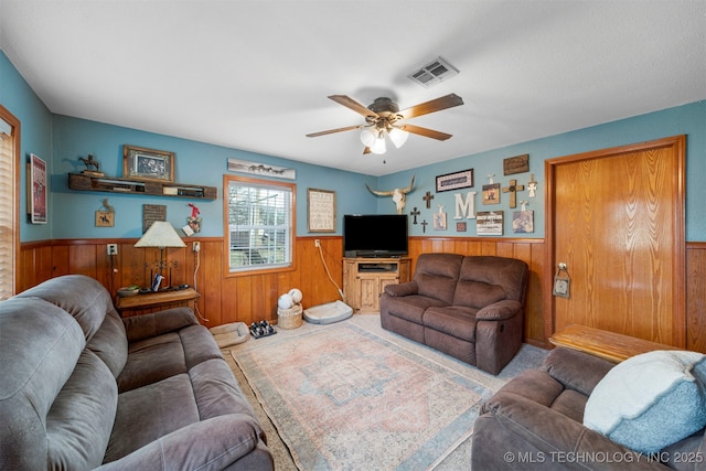 carpeted living room with ceiling fan and wood walls