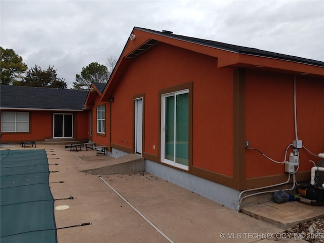 view of side of home with stucco siding, a covered pool, and a patio