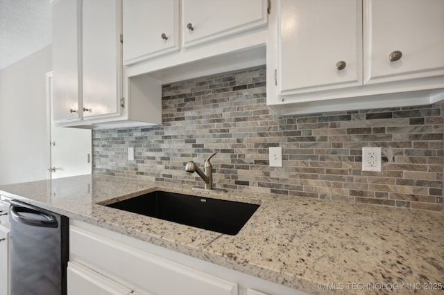 kitchen with tasteful backsplash, white cabinetry, sink, black dishwasher, and light stone countertops