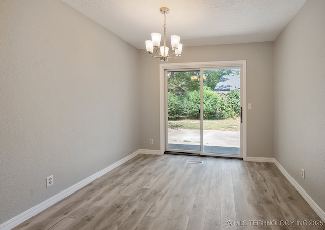 unfurnished room featuring a notable chandelier, a textured ceiling, and light wood-type flooring