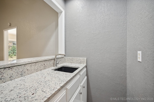 kitchen featuring light stone counters, sink, and white cabinets