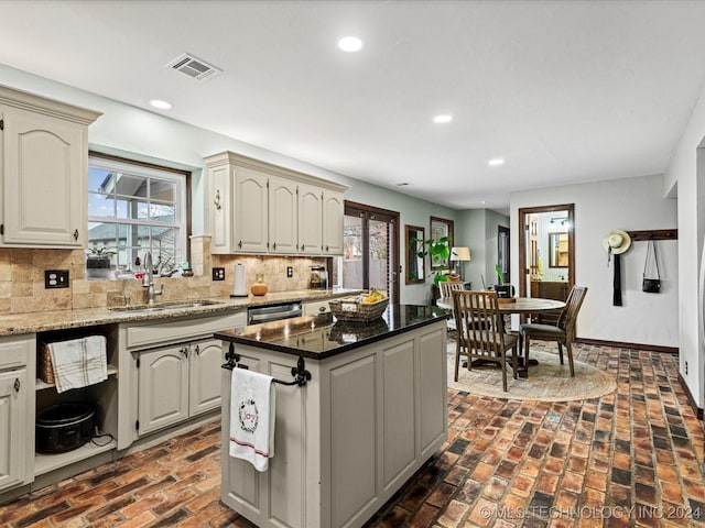 kitchen featuring backsplash, a healthy amount of sunlight, sink, dark stone countertops, and a kitchen island