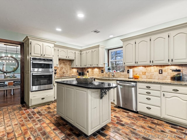 kitchen with sink, decorative backsplash, dark stone countertops, a kitchen island, and stainless steel appliances