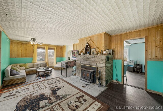 living room featuring hardwood / wood-style floors, a wood stove, ceiling fan, and wood walls