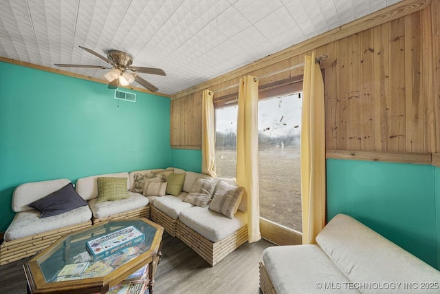 living room featuring hardwood / wood-style flooring, ceiling fan, and wooden walls