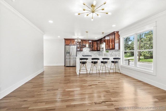 kitchen featuring a breakfast bar, backsplash, sink, stainless steel refrigerator with ice dispenser, and decorative light fixtures