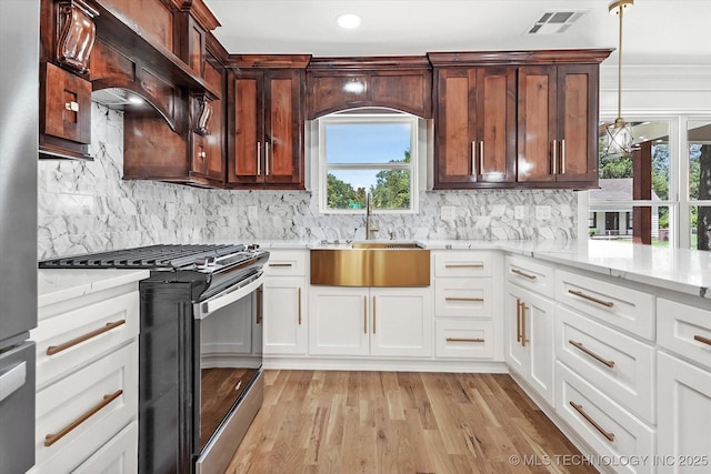 kitchen featuring sink, hanging light fixtures, stainless steel gas range oven, white cabinets, and custom exhaust hood