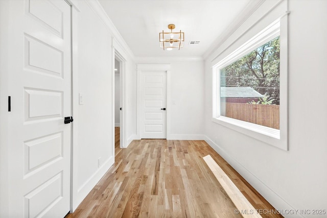 hallway featuring crown molding, a chandelier, and light wood-type flooring