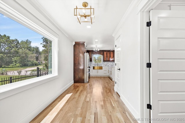 hallway with a chandelier, light hardwood / wood-style floors, crown molding, and a healthy amount of sunlight