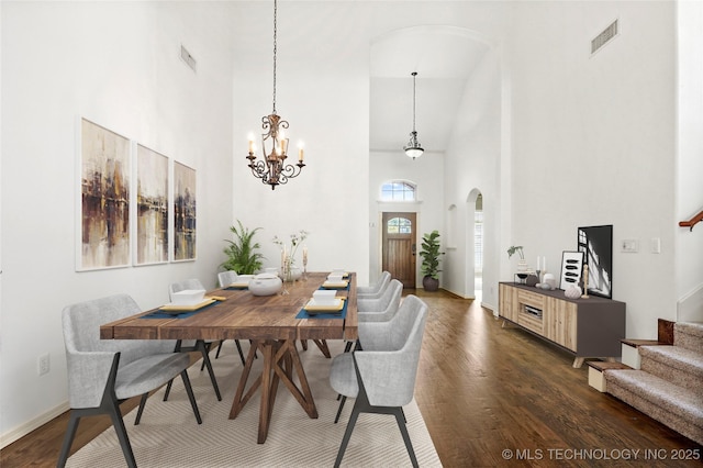 dining space with a towering ceiling, dark wood-type flooring, and a notable chandelier