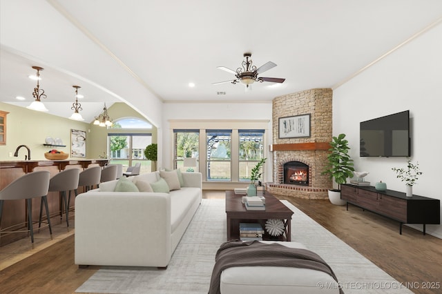 living room featuring a fireplace, wood finished floors, ornamental molding, and ceiling fan with notable chandelier