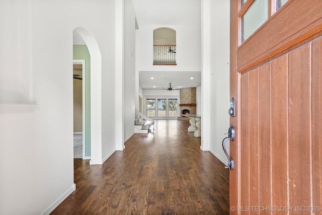 foyer entrance with stairway, a towering ceiling, baseboards, a large fireplace, and dark wood-style flooring
