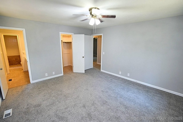 unfurnished bedroom featuring carpet, ensuite bath, ceiling fan, a spacious closet, and a closet