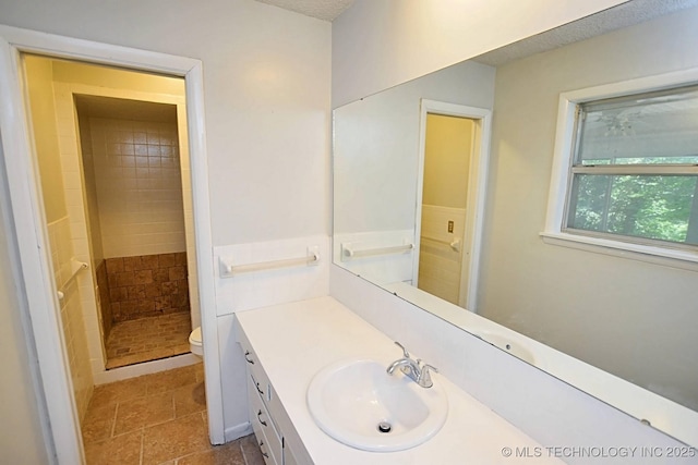 bathroom with a tile shower, vanity, and toilet