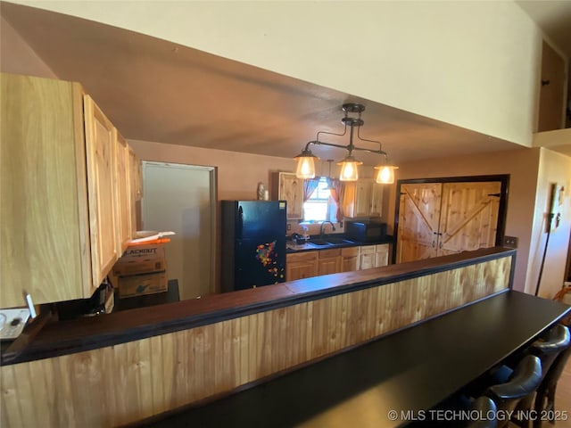 kitchen featuring pendant lighting, a kitchen breakfast bar, black refrigerator, and sink