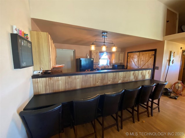 kitchen with kitchen peninsula, light hardwood / wood-style flooring, a breakfast bar area, and black appliances