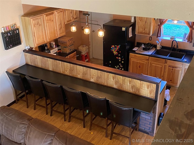 kitchen with pendant lighting, black fridge, sink, light hardwood / wood-style floors, and a kitchen bar