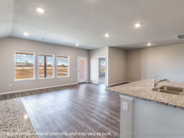 kitchen with lofted ceiling, a center island with sink, sink, dark hardwood / wood-style floors, and light stone countertops