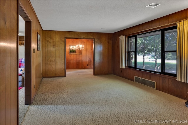 carpeted spare room with wooden walls, a textured ceiling, and a notable chandelier